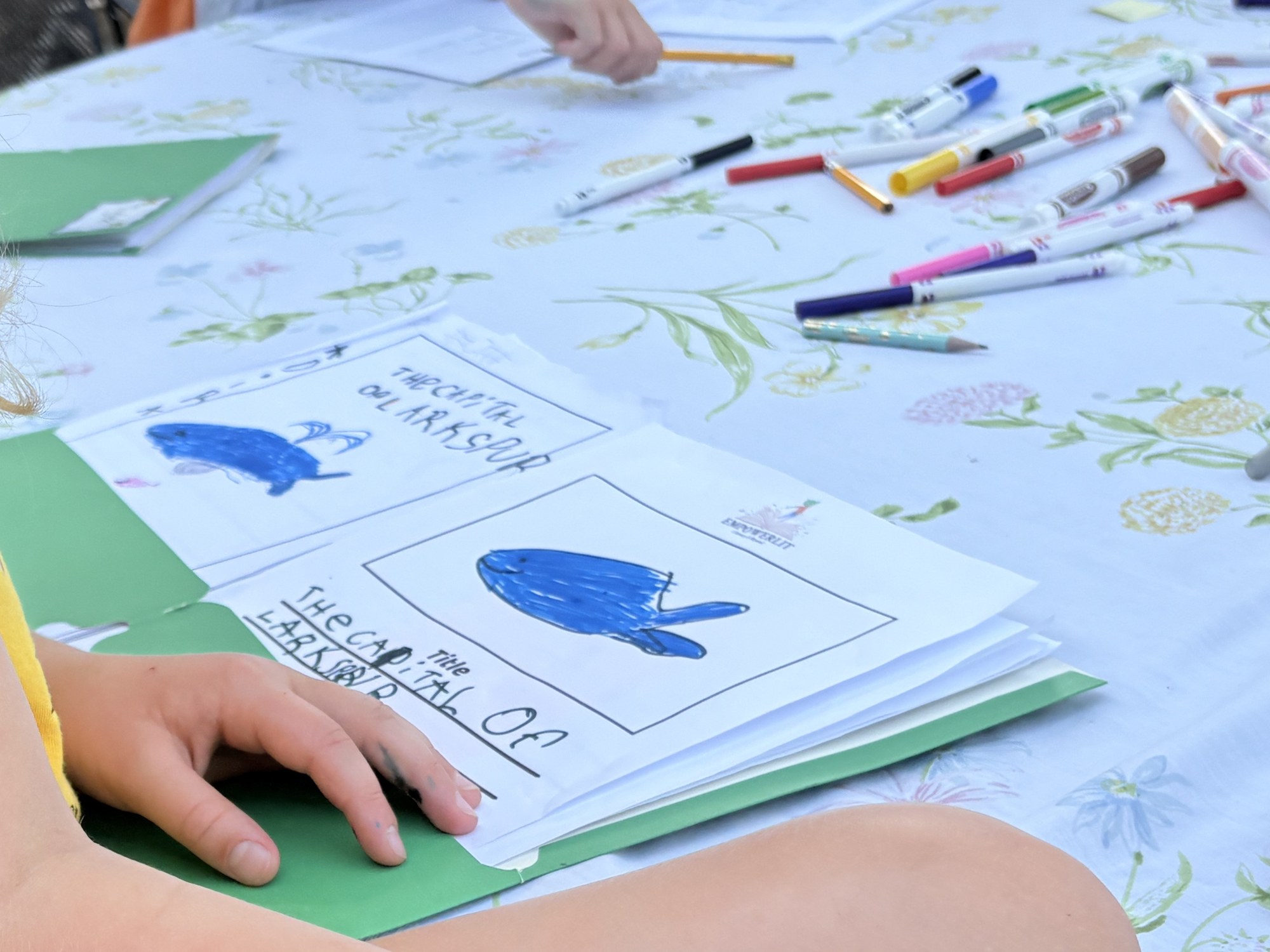 Student writing and illustrating their own storybook at a table of markers